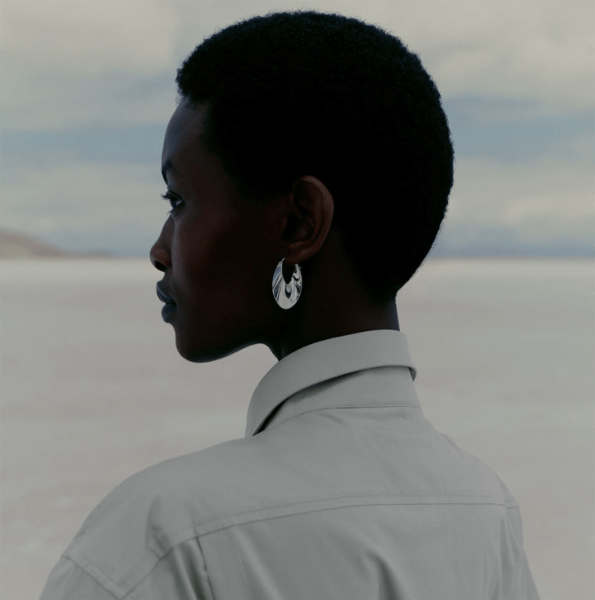 A woman wearing silver hoop earrings looks toward the sea