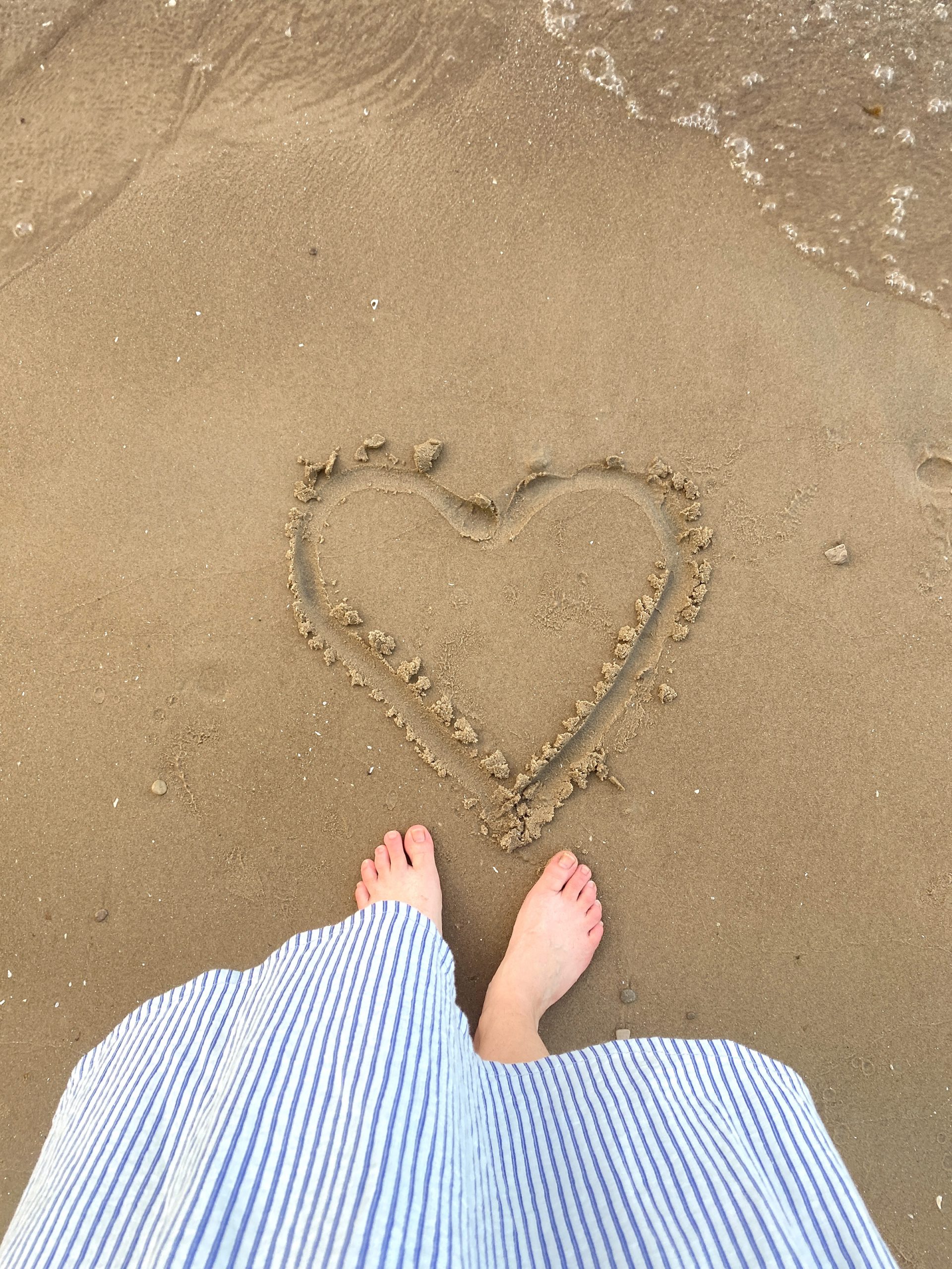 Bare feet and a heart shape drawn on sandy beach