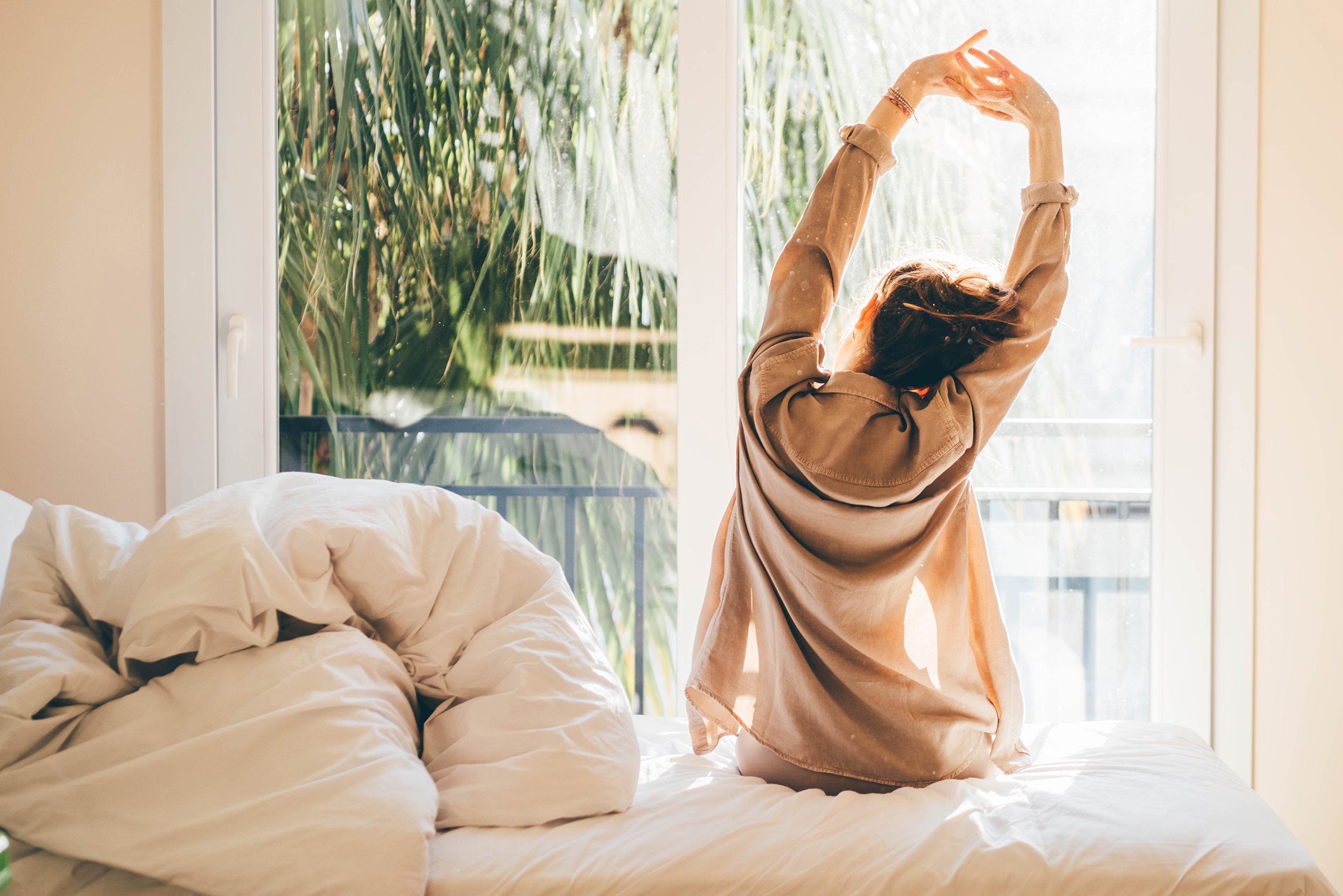 Woman waking up and relaxing near window at home.