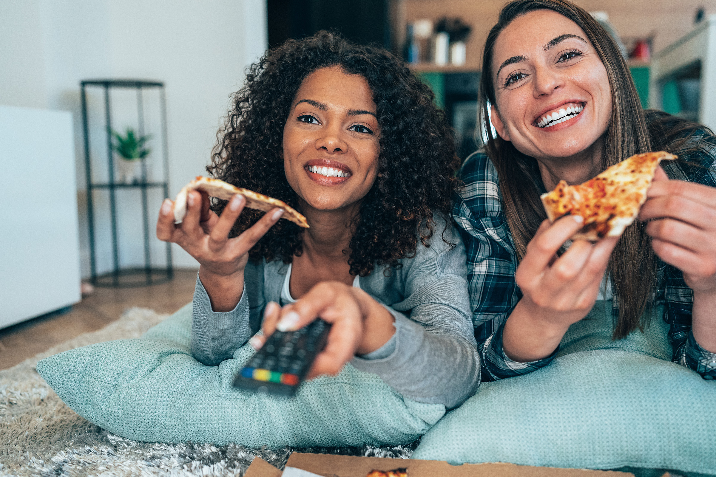 Two female friends eating pizza, watching tv and have a great time together at home