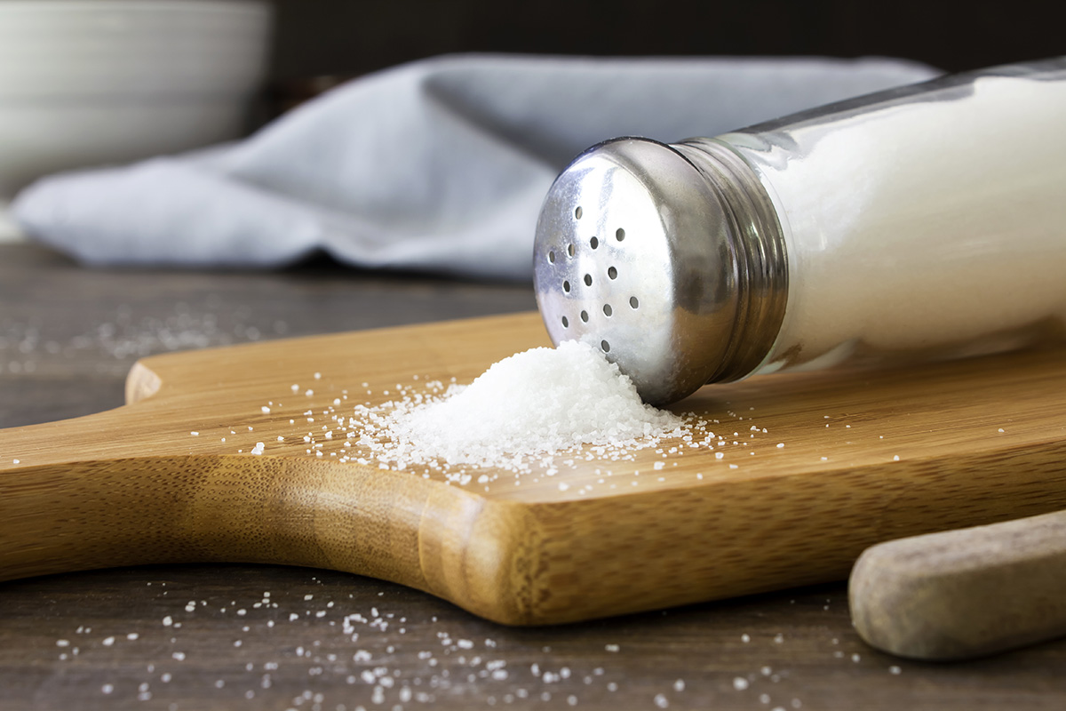 Salt spilling out of a salt shaker on a wooden chopping board