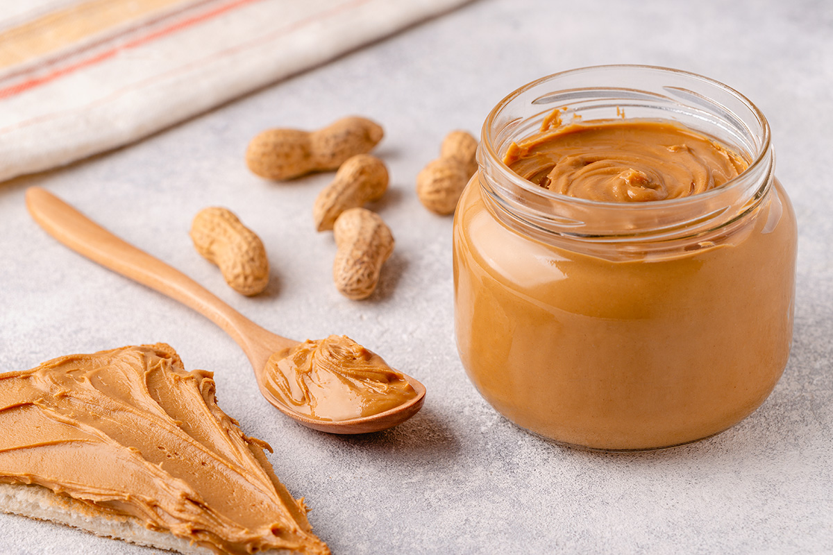 A jar of peanut butter next to a spoonful of peanut butter and half a slice of toast covered in peanut butter