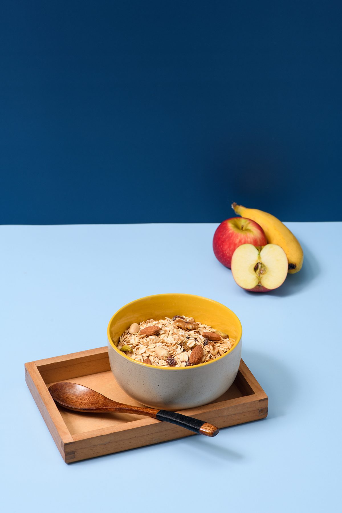 A bowl of oatmeal, an apple, and a banana against a blue background