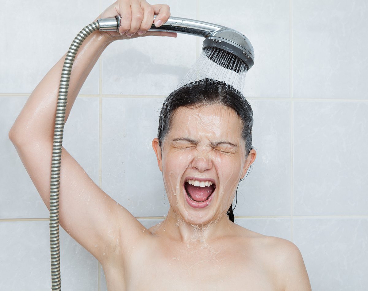 A woman is screaming in the shower, holding the shower head above herself