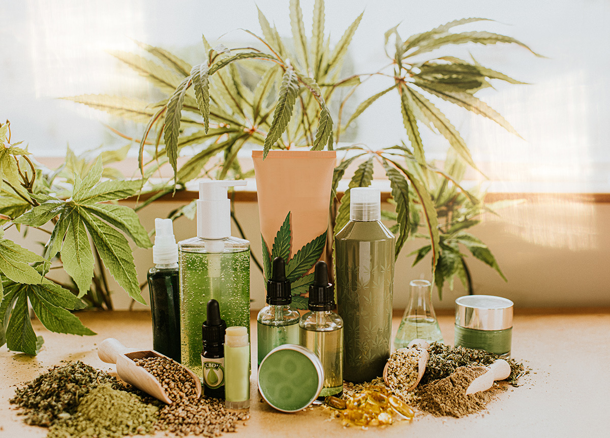 A selection of CBD products, including gels, creams, oils and balms, and hemp seeds in front of hemp leaves