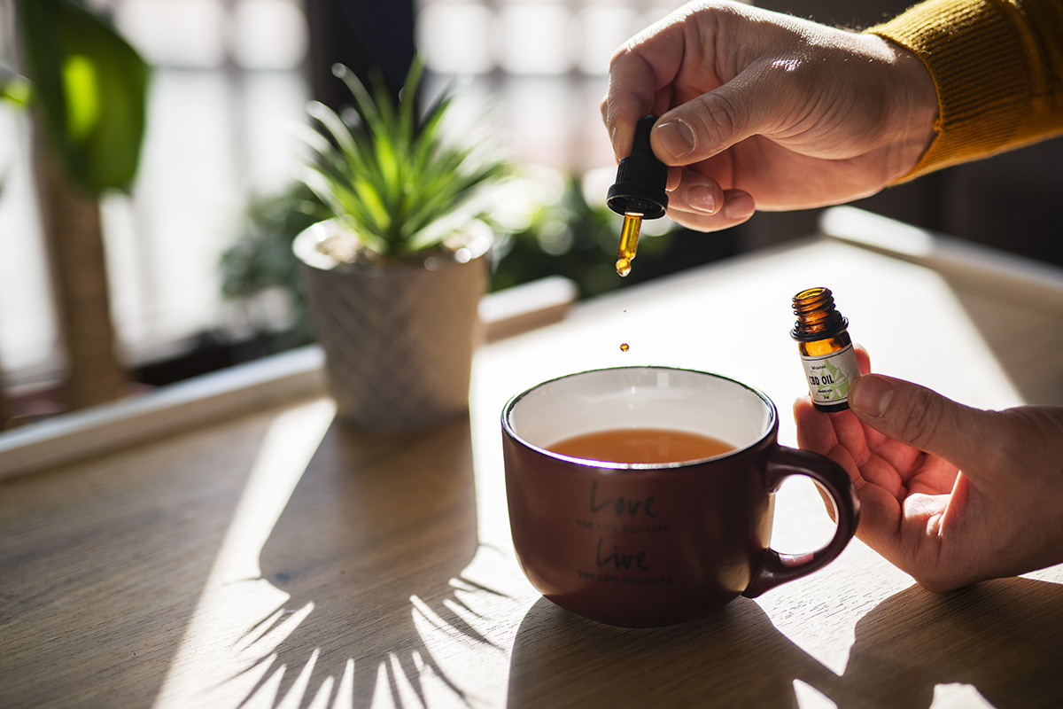 A hand adding CBD oil to a mug of tea