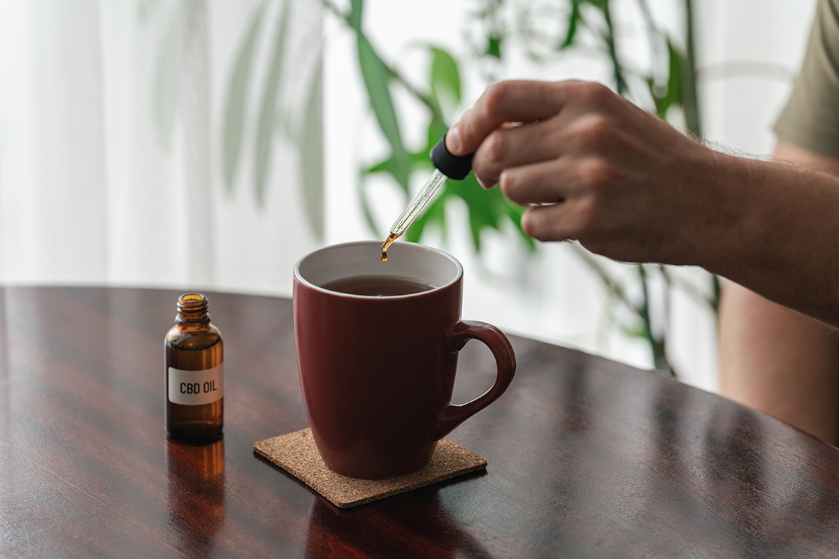 A hand adding CBD oil to a hot drink