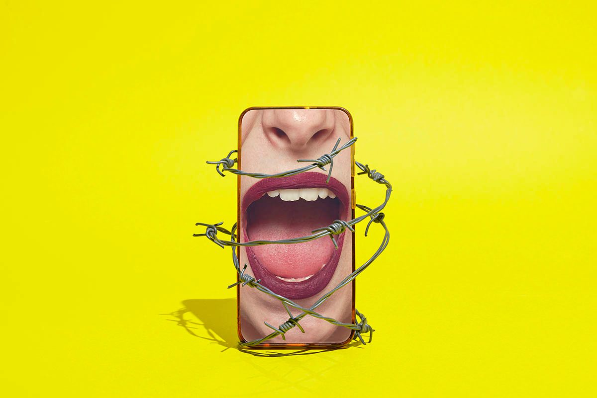 A smartphone displaying an image of a women's mouth, which is open to suggest she's talking, is wrapped in barbed wire against a bright yellow background.