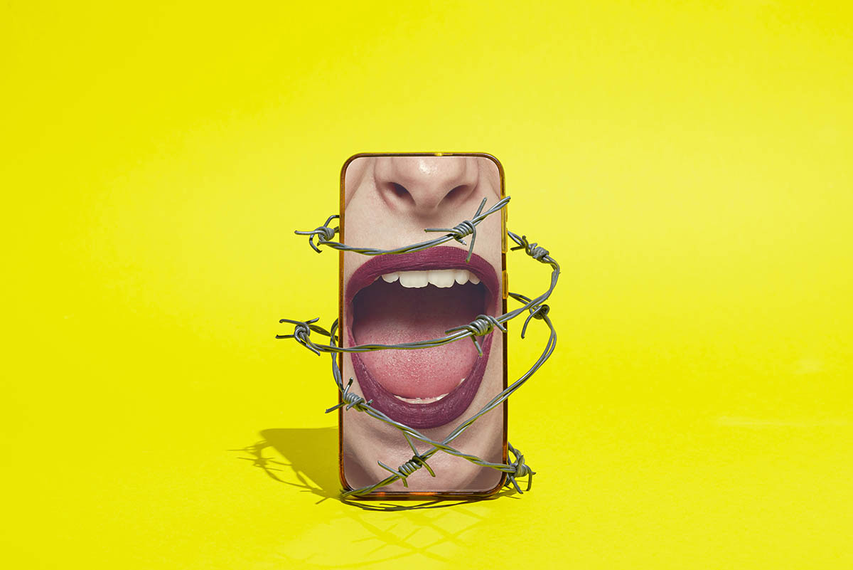 A smartphone displaying an image of a women's mouth, which is open to suggest she's talking, is wrapped in barbed wire against a bright yellow background.
