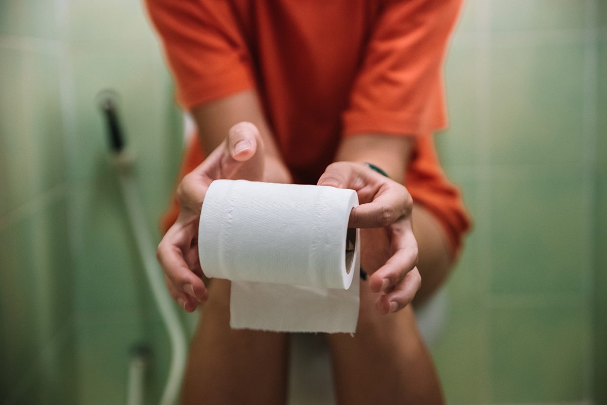 A woman sits on the toilet holding a roll of toilet paper 