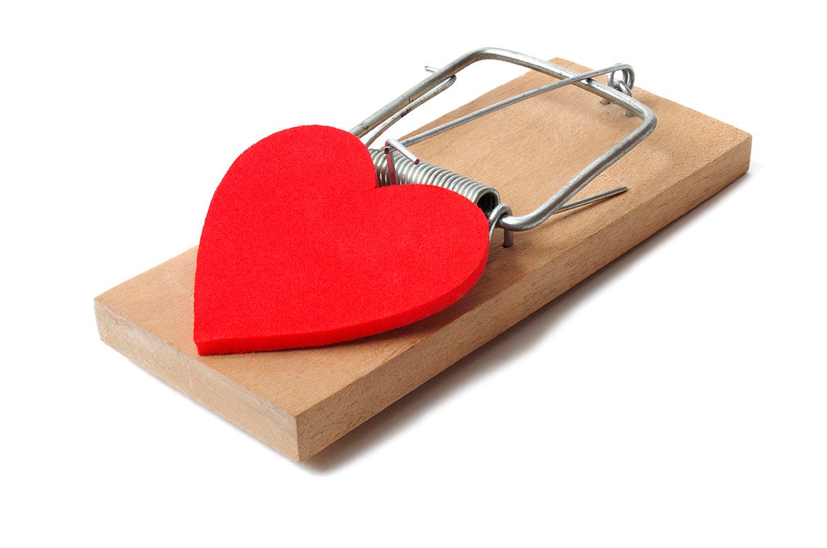 A red heart sits on top of a mousetrap against a white background