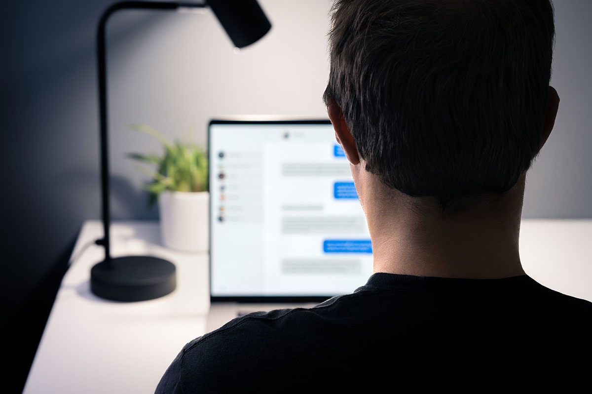 A man sits at a laptop in a dimly lit room