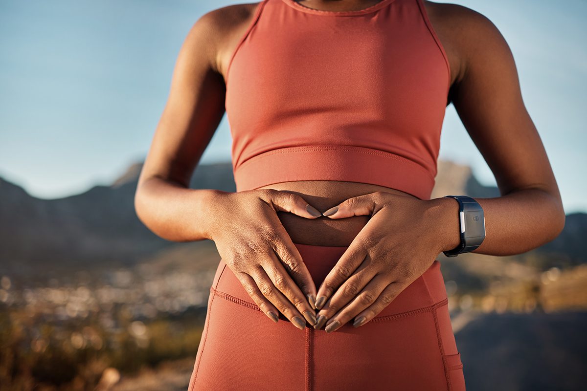 A woman wearing activewear has her hands on her stomach, with her fingers creating a triangle shape.