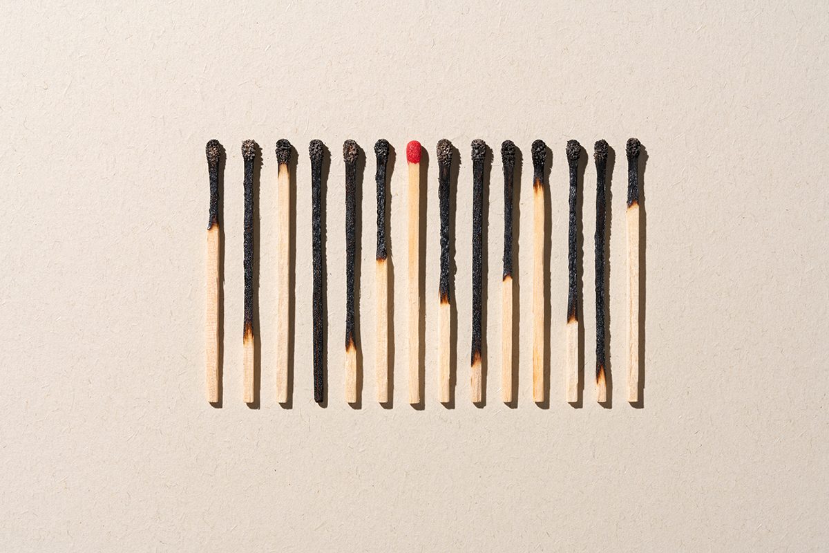 A line of burnt matchsticks with one matchstick that hasn't been burnt in the middle are set against a beige background.
