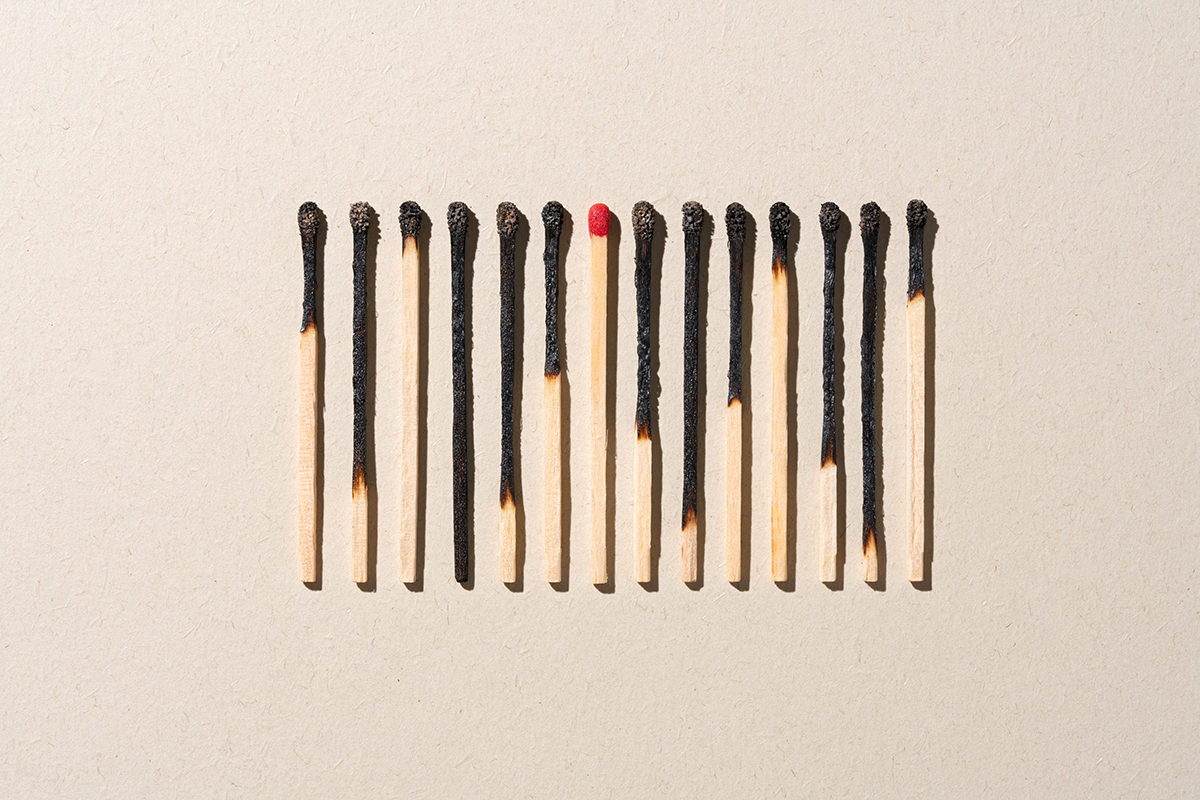 A line of burnt matchsticks with one matchstick that hasn't been burnt in the middle are set against a beige background.