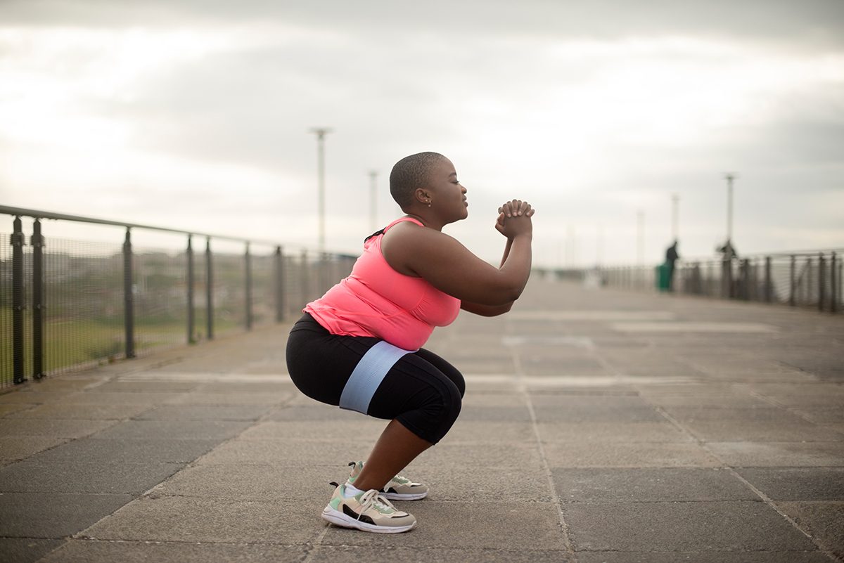 A woman is doing a squat using a resistance band outside.