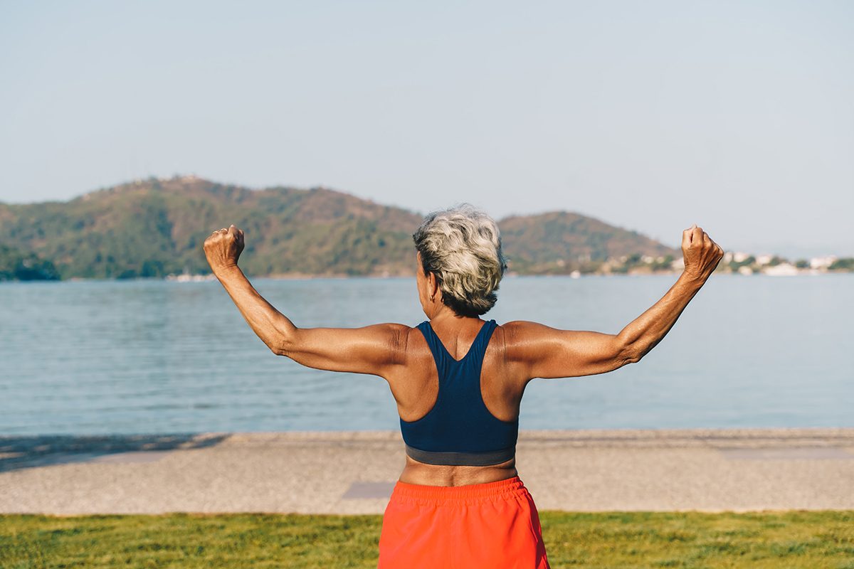 A woman raising her arms triumphantly next to a body of water