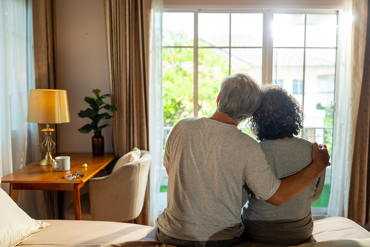 A senior couple sitting on a bed, leaning against each other