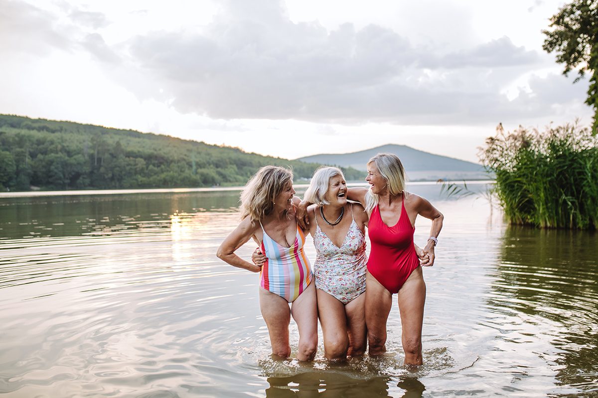 Three mature women are embracing and laughing while standing in a lake