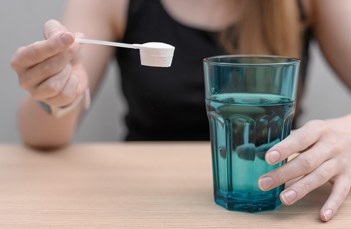 A woman is about to dissolve a scoop of creatine powder in water