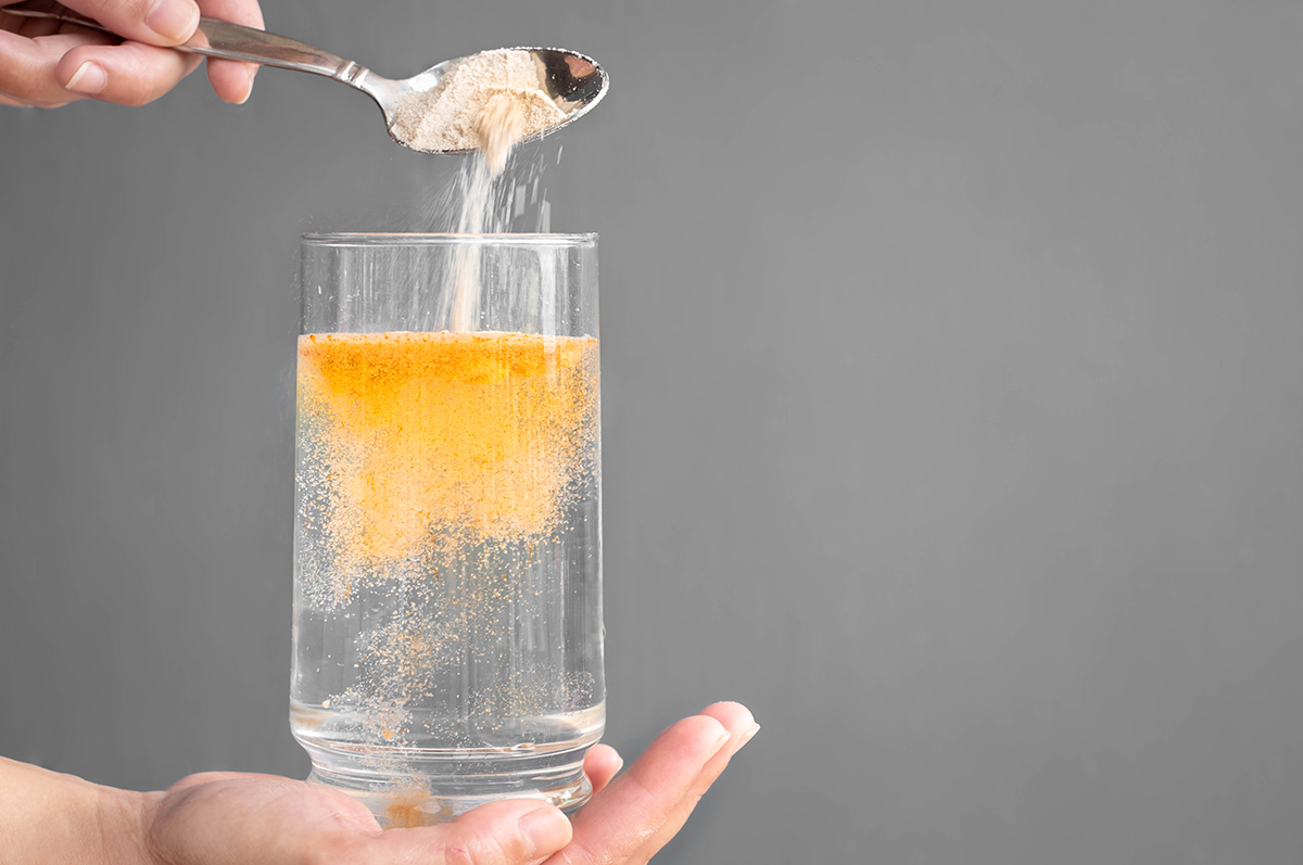 A person pours a spoonful of orange powder into a glass of water.