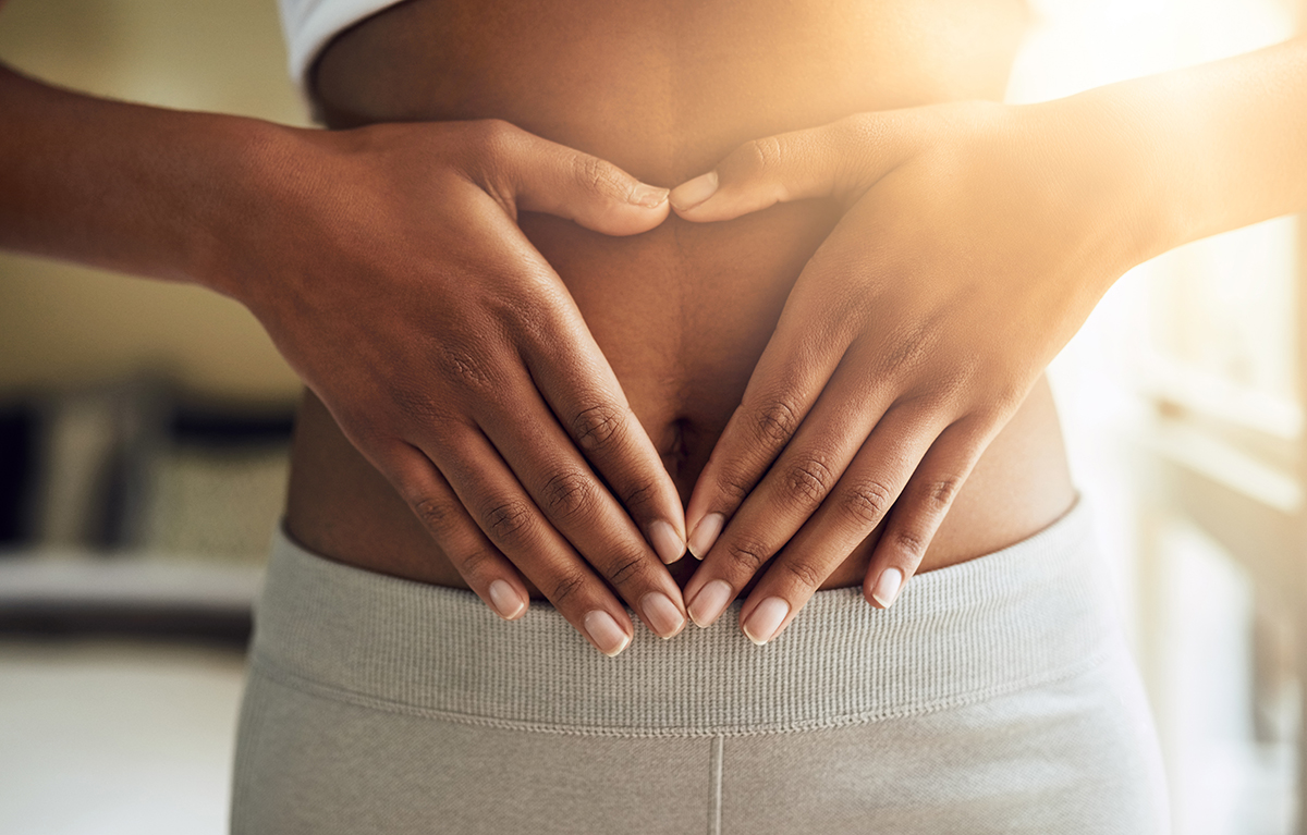 A cropped shot of a woman making a triangle shape around her belly button with her hands.