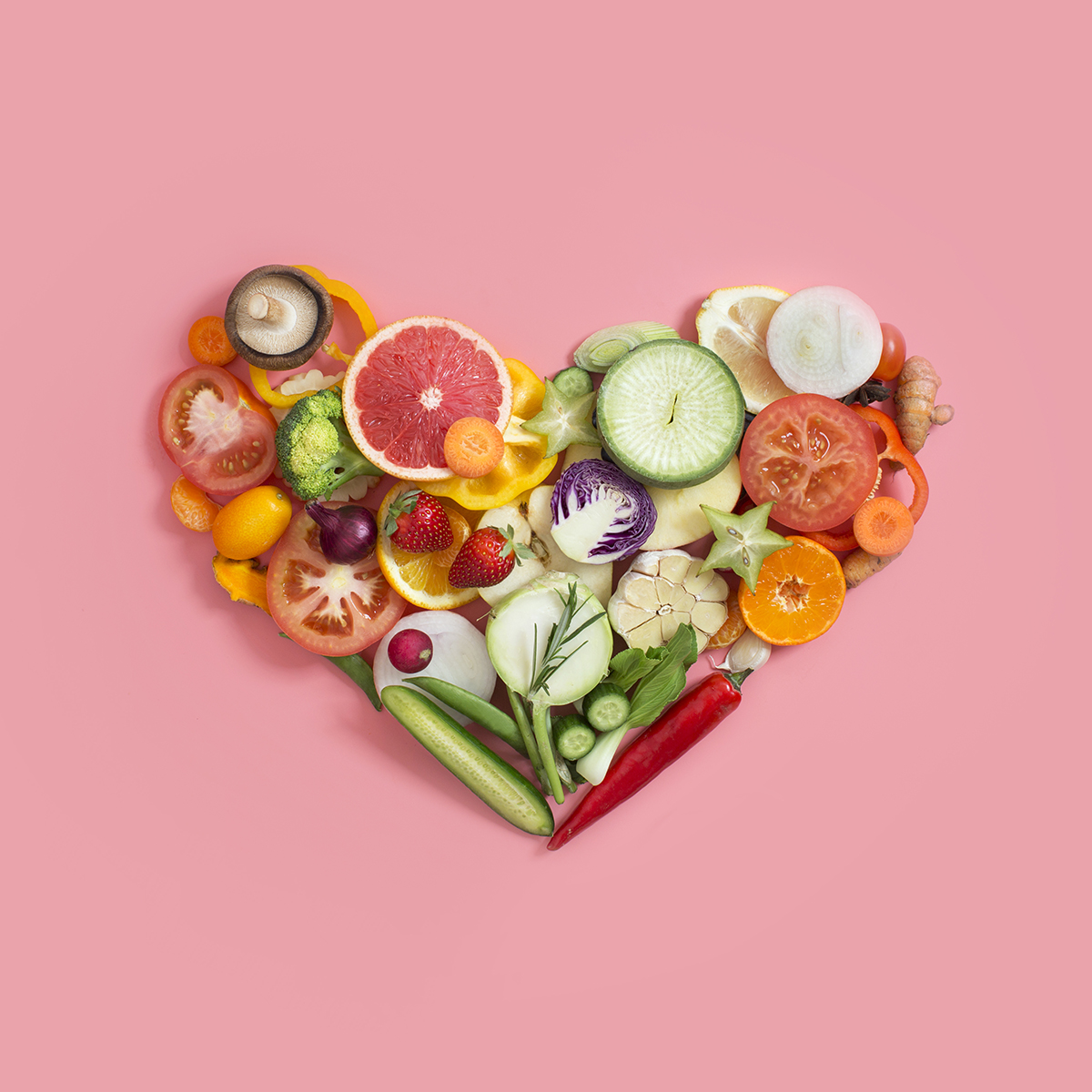 Fresh fruit and vegetables arranged in the shape of a heart on a pink background
