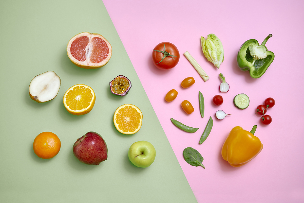 An assortment of fruits and vegetables, some cut in half, on a green and pink background