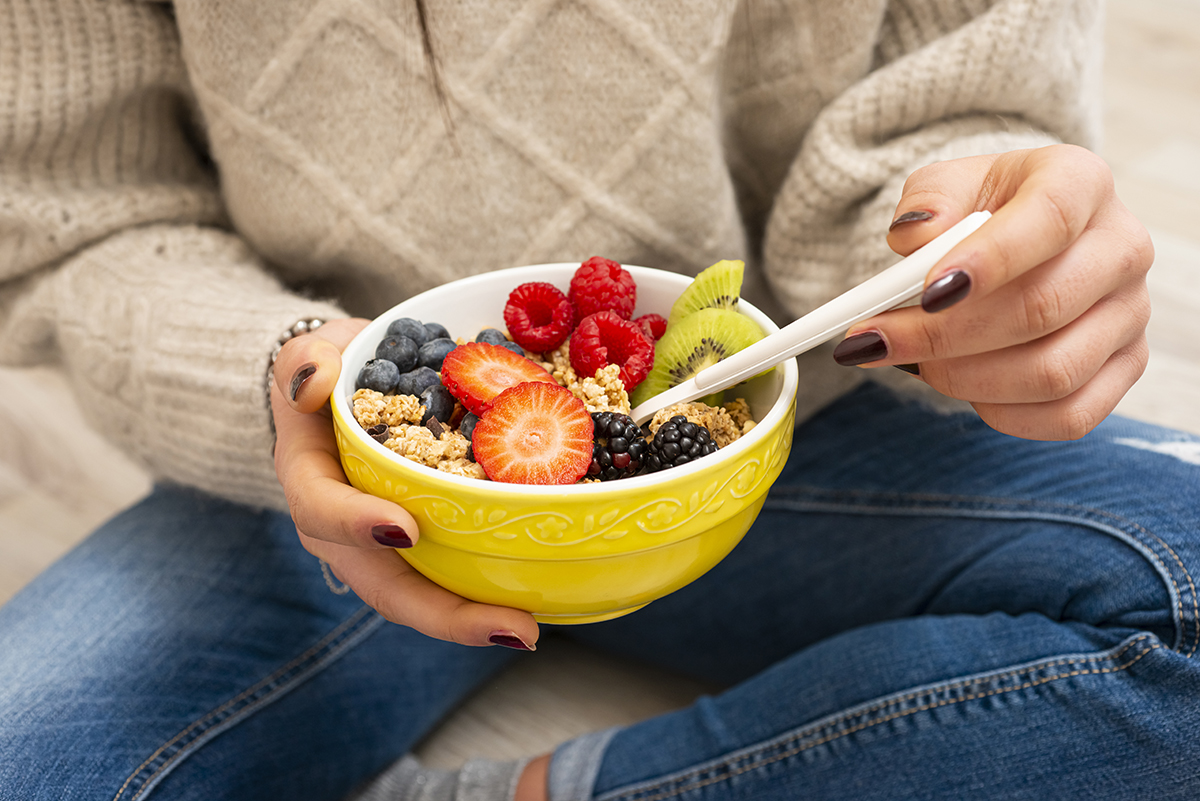 A woman holding a bowl containing granola and fresh fruit