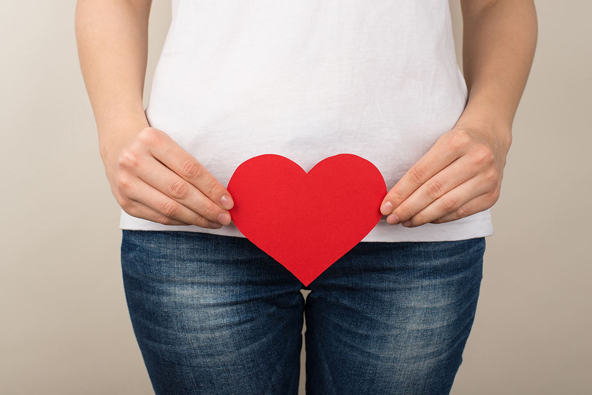 A cropped shot of a woman holding a heart cutout near her crotch