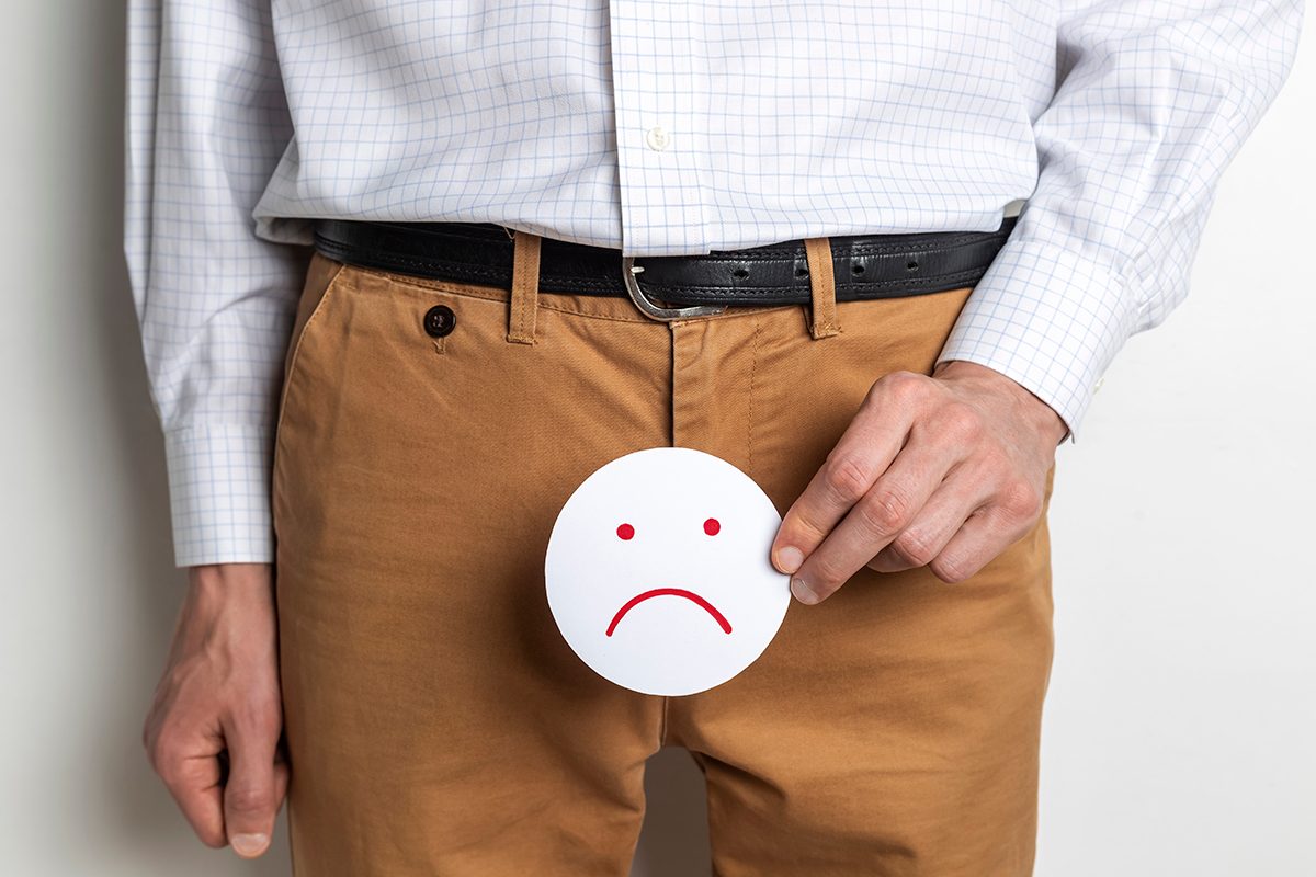 A man holding a sad face cutout in front of his groin