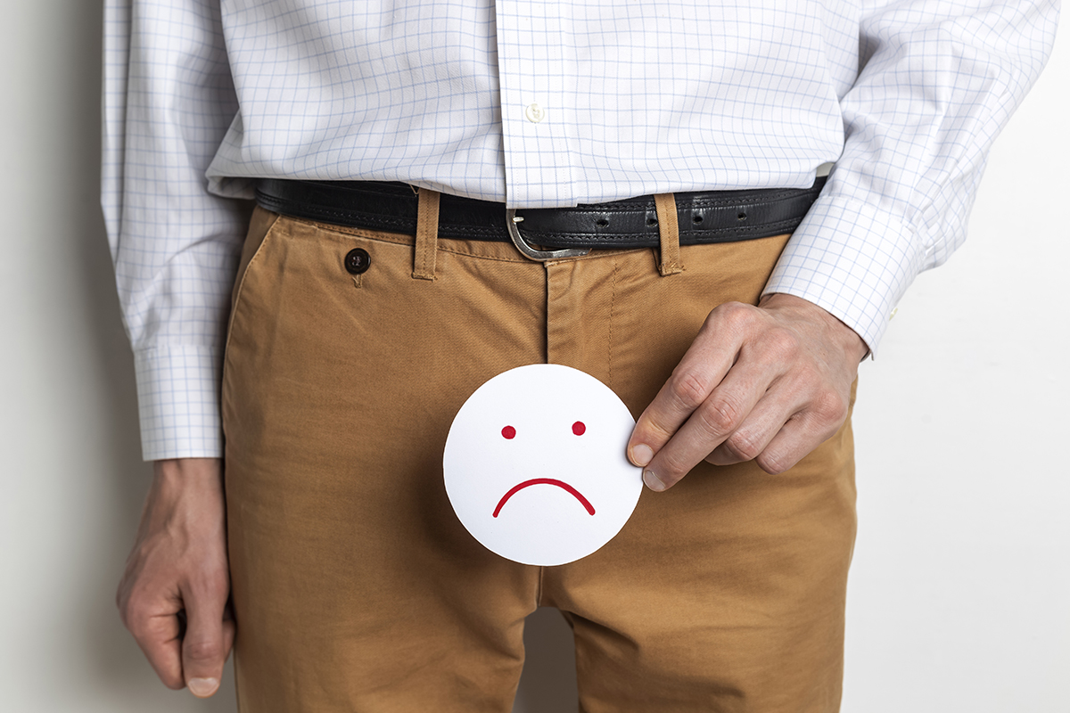 A man holding a sad face cutout in front of his groin