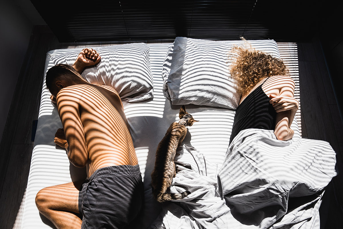 A couple sleeps with their backs turned to one another on opposite sides of the bed