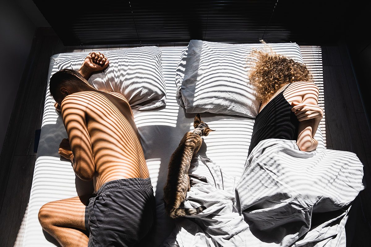 A couple sleeps with their backs turned to one another on opposite sides of the bed