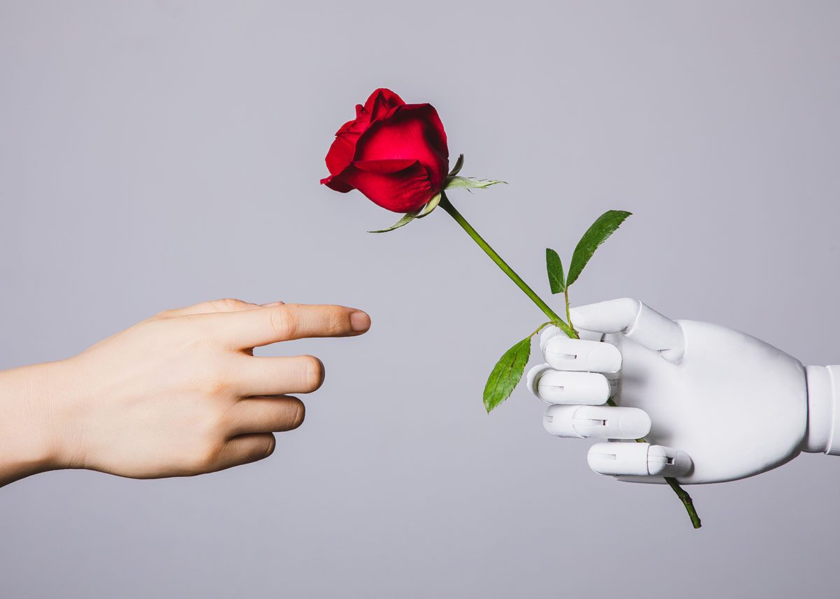A human hand reaches out to a robot hand holding a red rose