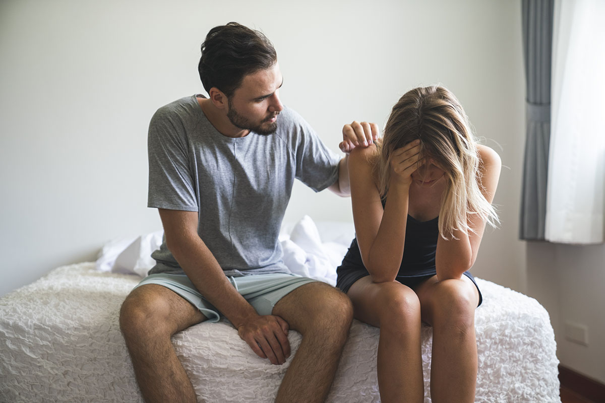 A visibly upset couple sit on the end of a bed