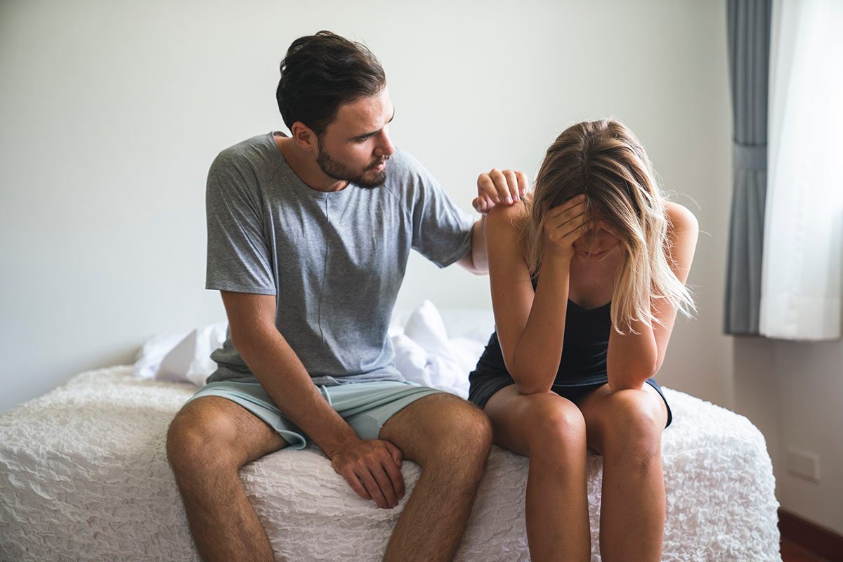 A visibly upset couple sit on the end of a bed