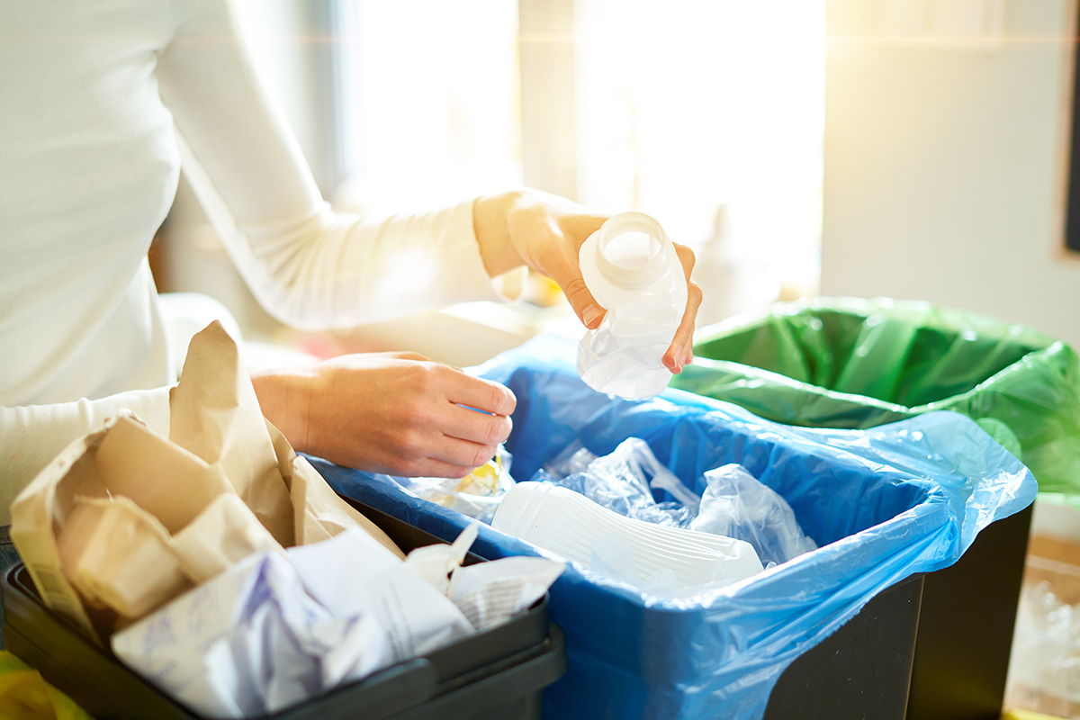A close up view of hands sorting recycling into three black recycling bins.