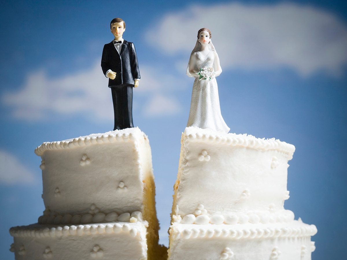 A wedding cake is split in two, with a groom figurine on one half and a bride on the other, symbolising divorce