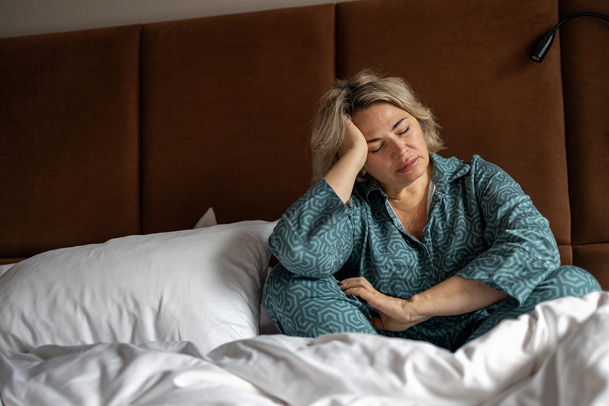 A woman sits on her bed, resting her head on her hand