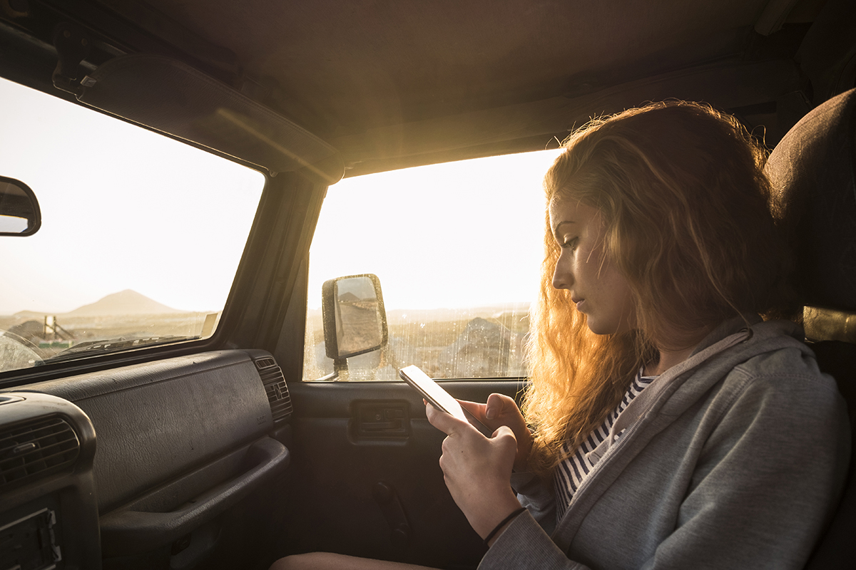 A woman sitting in the passenger seat of a car, using a mobile phone