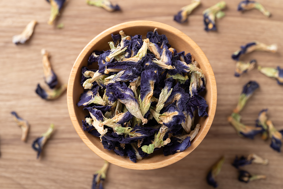 A wooden bowl containing dried butterfly pea flowers on a wooden surface