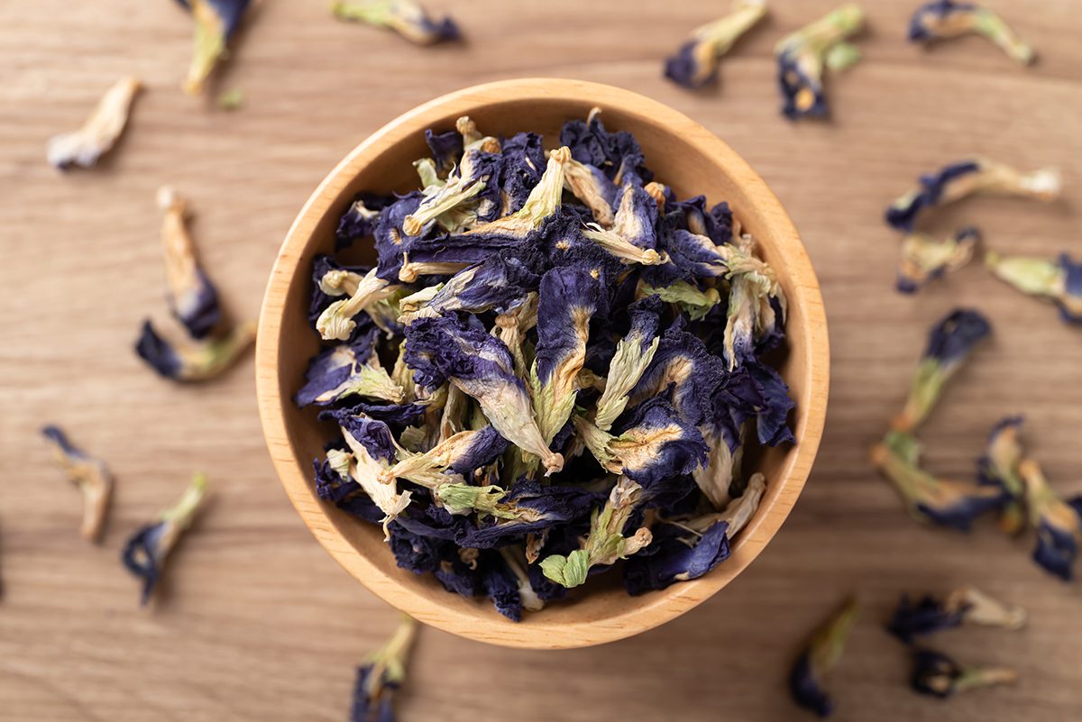 A wooden bowl containing dried butterfly pea flowers on a wooden surface