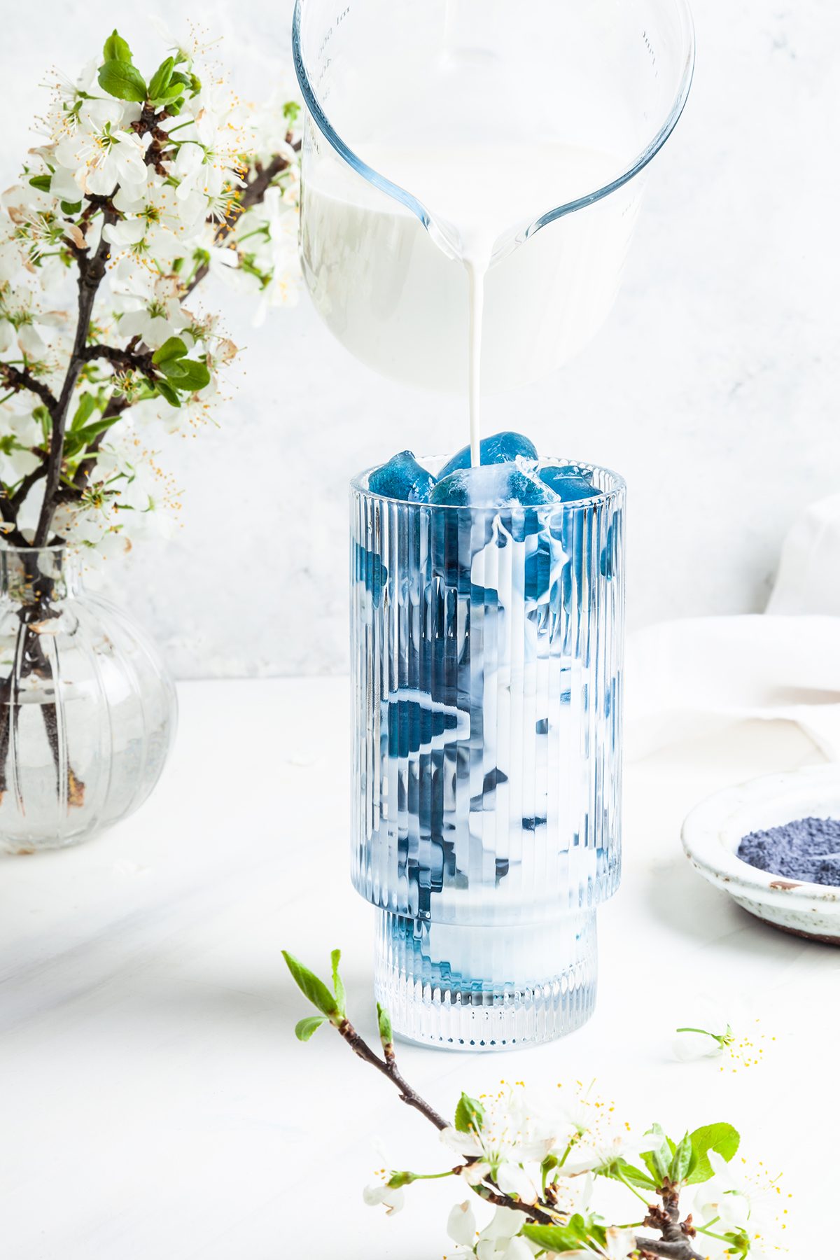 Milk being poured over ice into a blue matcha latte, against a white background
