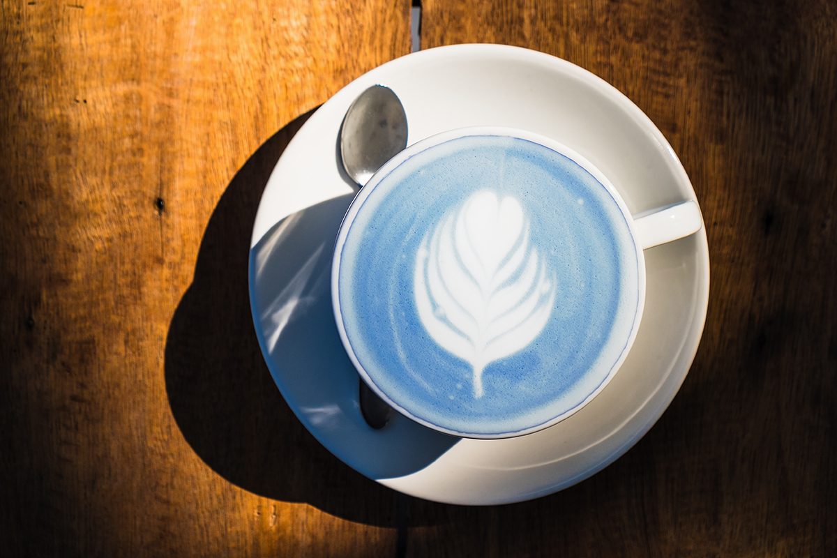 A blue matcha drink with latte art sits on a wooden surface