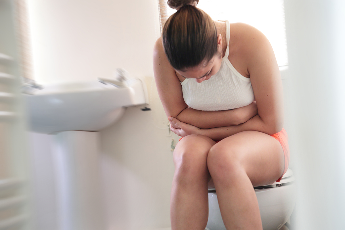 A woman sitting on a toilet holding her stomach in pain
