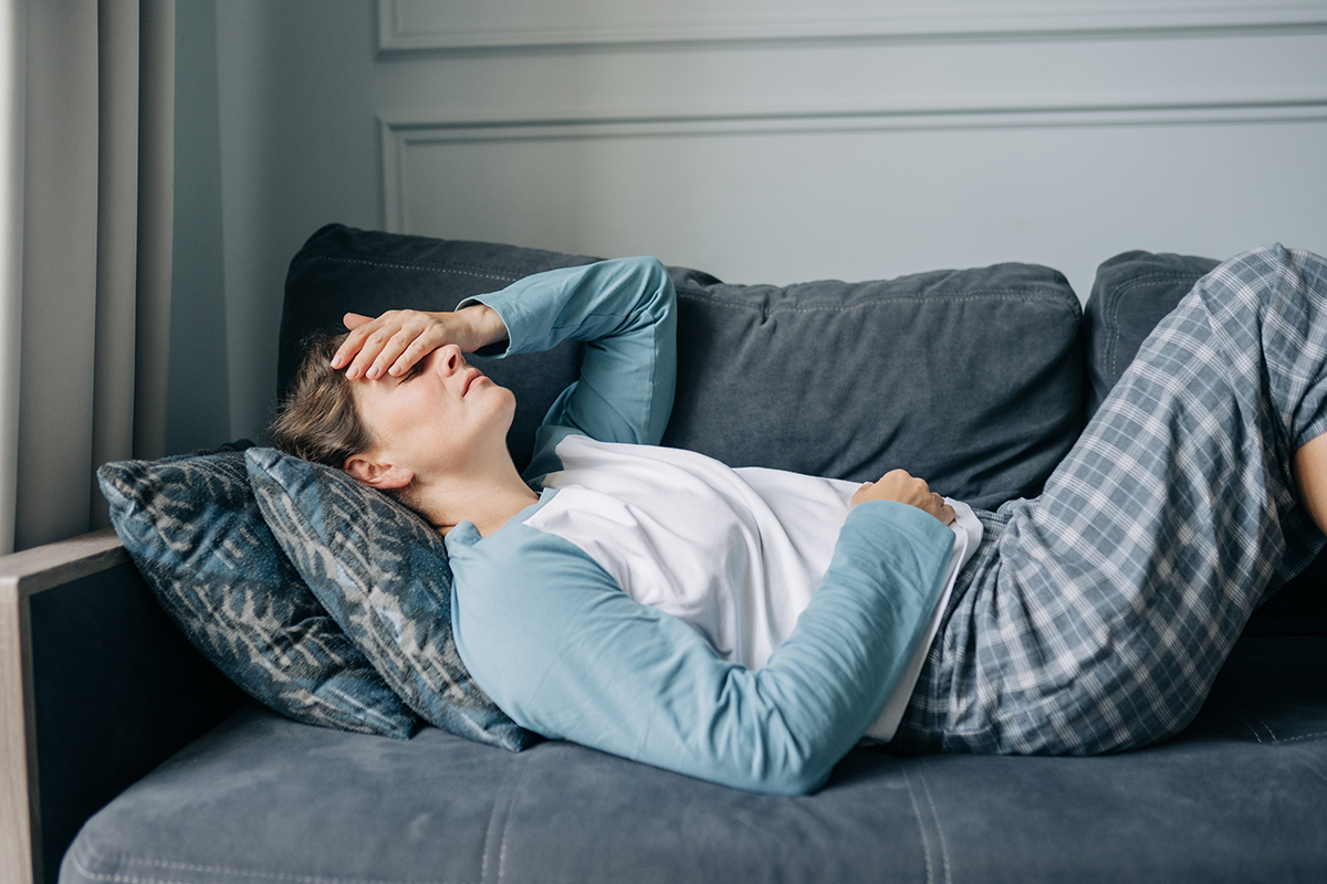 A woman is lying on the sofa covering her forehead with her hand, suggesting she has a headache