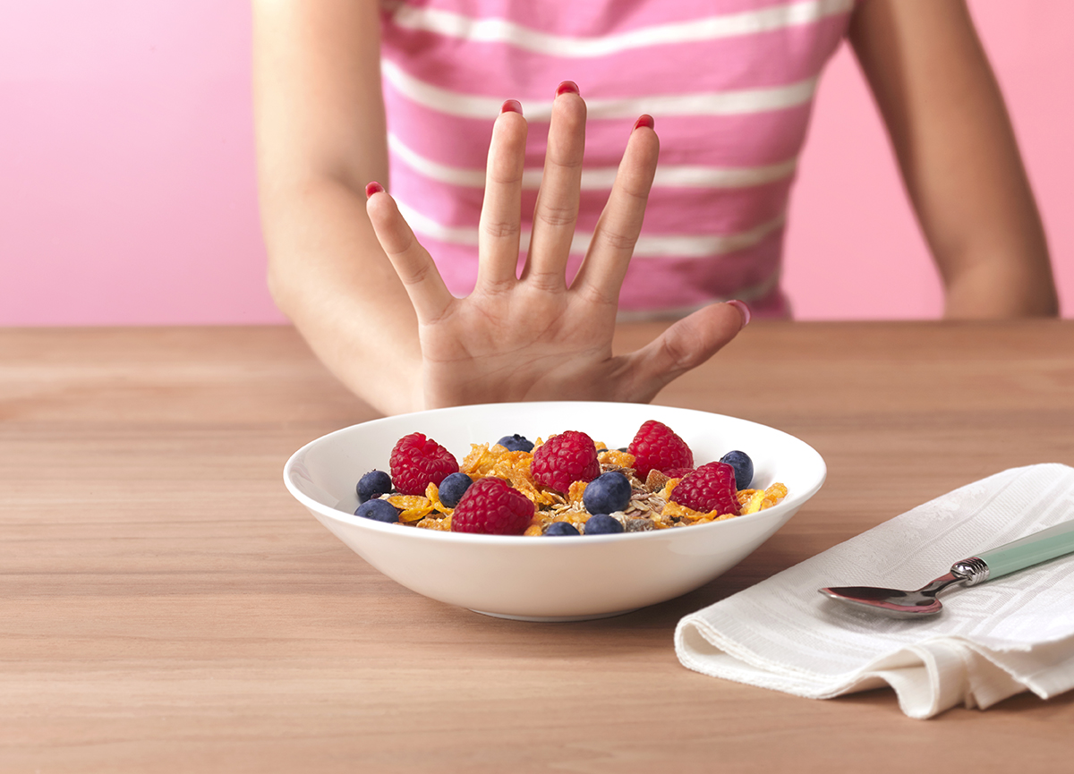 A girl holding her hand up to a bowl of cereal and berries