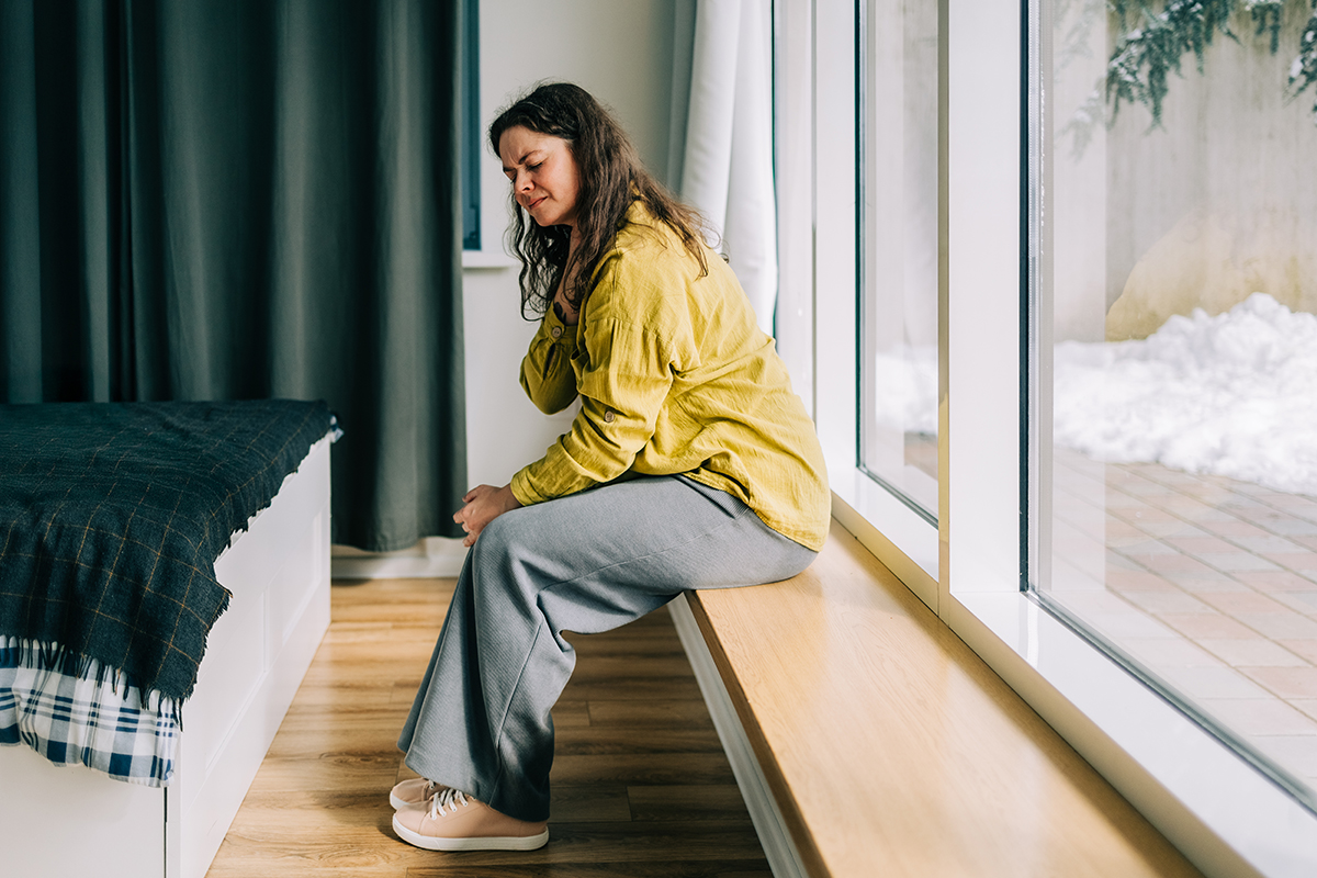 A woman sitting on a windowsill, touching her throat