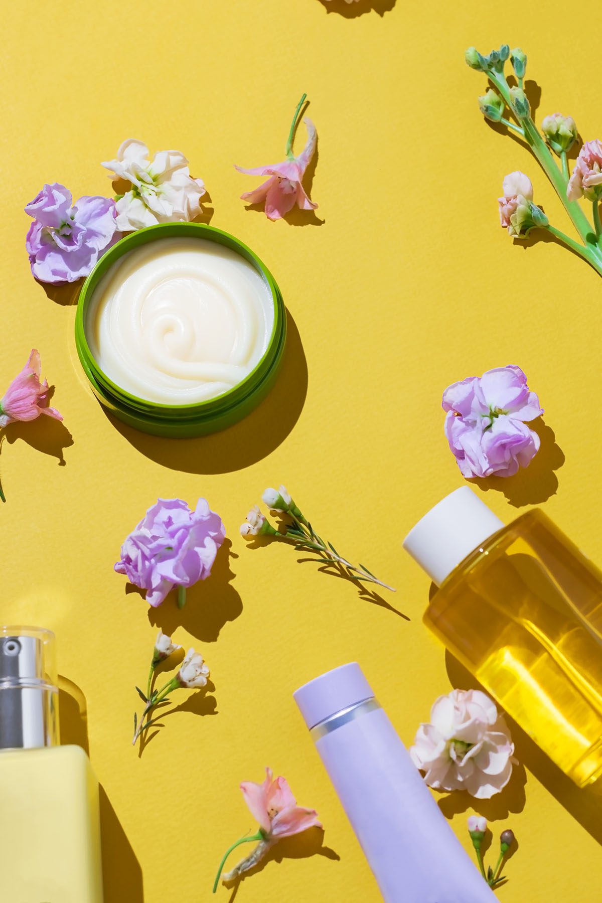 Skincare products surrounded by flowers on a yellow background